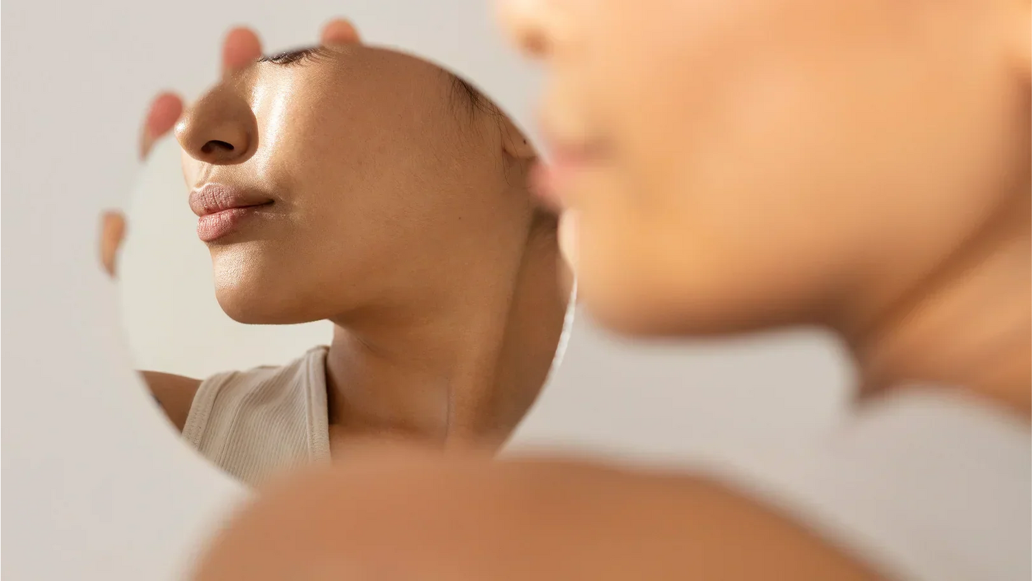 Une femme se regarde dans un miroir, réfléchissant à des moyens de raffermir sa peau.