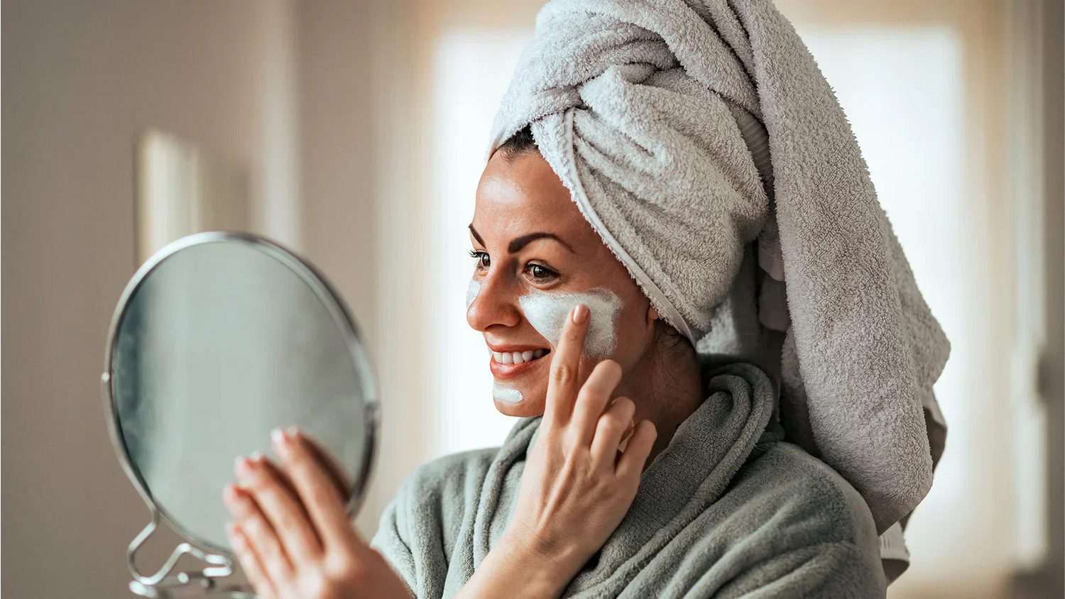 Une femme en serviette examine son visage dans le miroir, mettant en avant des soins visage.